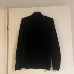 Stickad tröja  - En fin tröja till vardagen med en detalj av en rand som går igenom hela tröjan. Från arma till arm. Har en liten krage men den syns inte när man har på sig tröjan. Svart med en rand som är vit/beige
