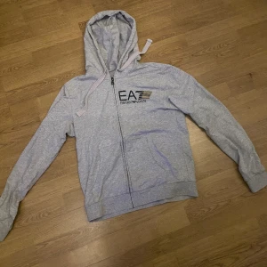Armani zip hoodie - En riktigt fet Armani zip hoodie som är in 7/10 skick, allt pågrund av ett pytte litet hål i luvan som man inte ser(ringat in den på bilden)Tror jag köpte den för 1250kr, men säljer den billigt för att bli av med den.