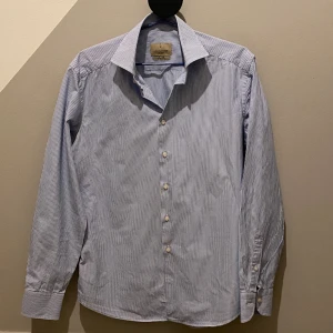 Lachemise Skjorta  - En stilren skjorta från Lachemise i en snygg ljusblå randig färg. Skjortan är i bra skick. Alla knappar är kvar! Slim fit. 100% Bomull  Hör av er vid frågor eller funderingar! 