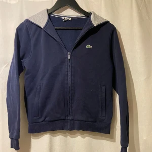 Lacoste Zip Hoodie - ▪️Lacoste zip hoodie i färgen  🔹Marinblå🔹 ▪️Skick 10/10 använd fåtal gånger (nyskick) ▪️Nypris: 800kr ▪️Vårt pris: 349kr (priset kan diskuteras)
