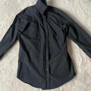 Svart skjorta  - Säljer denna skjortan då jag aldrig använder den storleken är L. En knapp vid armen har lossnat. Köpt för 400kr