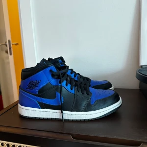 Nike Air Jordan Mid blå/svart Strl 42 - Nike Air Jordan 1 Mid i blått och svart. Skorna är i gott skick och har inte använts mycket. 