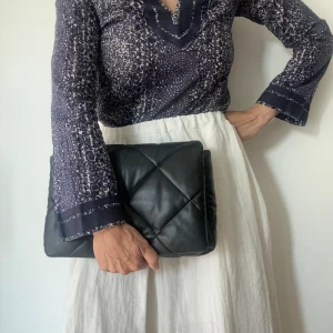 Wanda mini quilted faux leather shoulder bag - Snygg väska från Stand Studio i svart, quiltad läderimitation. Väskan har ett avtagbart handtag och en avtagbar axelrem i samma färg. Kan bäras i handen, som crossbody eller som clutch. Stängs med lock och magnetlås. Axelrem och dustbag medföljer.