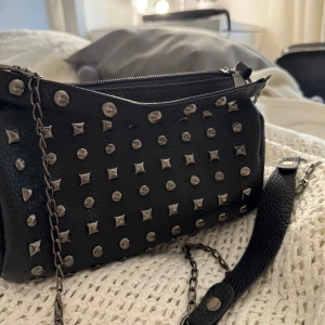 Väska - Svart väska med nitar omkring. Säljer då jag har flertal väskor, små fickor inuti och massor med rum. Priset kan diskuteras vid snabbt köp! Tryck gärna på köp nu 💕