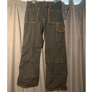 Svart orangea jobb byxor - Jobb byxor, svarta med orangea detaljer. Storleken är 50, dock sjukt små så vet inte hur accurate de är