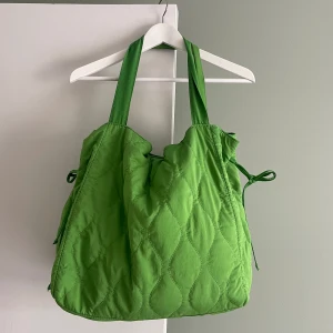 Grön stor väska - Grön stor väska från Gina Tricot. Fint mönstrad. Dragsko upptill som gör den lätt att anpassa efter hur mycket man behöver packa med sig. Väldigt rymlig, har ett stort fack och tre innerfack varav en med dragkedja.  Använd och omtyckt, i gott skick!