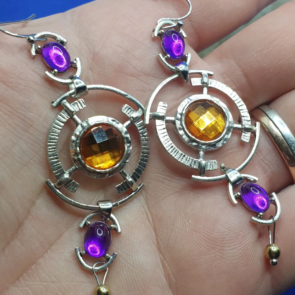 Den här örhänget föreställer örhängen och måtten är ca 6.5×3 cm. Silverfärgad metall med vacker ytstruktur och kristaller i vackra färger bl.a. Oerhört vackra örhängen av hög kva. Asusteet.