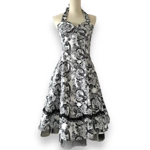 Klänning i rockabilly-stil med döskallar - Superfint skick! Från Hearts & Roses London. Halterneck knytning. Spets detalj samt tyll i nederkant. Obs! Den är märkt som storlek 12/40/L men jag uppfattar den som mindre. På bilden har skyltdockan XS/S och den sitter bra på mig som brukar ha S.