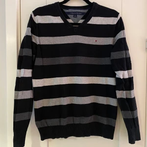 Svart och grå randig stickad v-ringad tröja från Tommy Hilfiger i strl M - Mått Över axeln: ca 42 cm Längd från axeln och ner: ca 66 cm  Använd men i bra begagnat skick.  Kommer från ett djur och rökfritt hem.