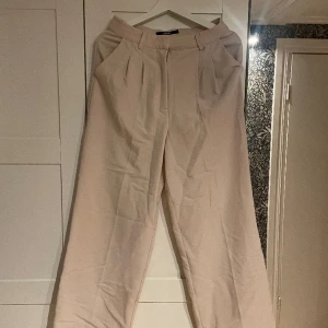 Beiga kostymbyxor   - Ett par beiga kostymbyxor, i bra skick, utsvängda vid foten och högmidjade. 