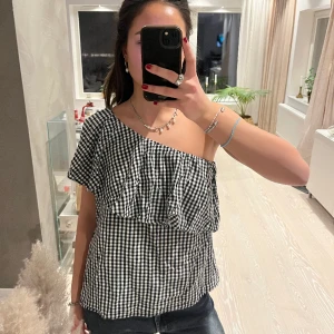Enärmad rutig topp - Enärmad topp som är rutig svart och vit. Bea skick. Storlek M men passar också S.