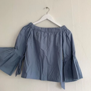 Blå off-shoulder topp med vida armar - Band knyts vid ärmarna.