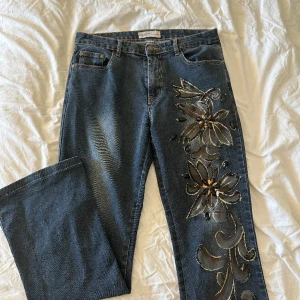 Lågmidjade jeans  - Lågmidjade jeans med coola detaljer i en bootcut modell.  Finns lite slitage från paljetterna från blomman på benet. Storlek L men är mer en M  Midjemått: 39cm 