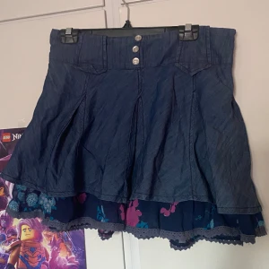 mörkblå kjol - en jättefin kjol som aldrig har kommit till användning. blommorna i det undre tyget har glitter på sig. samfraktar gärna med andra saker! midjemåttet ligger på runt 84 cm. 