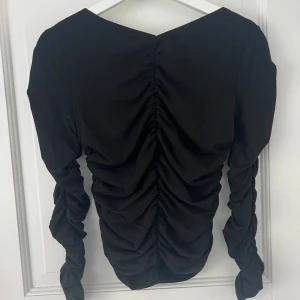 Svart topp  - Svart långärmad topp från NA-KD i storlek M. Sömmarna gör tröjan mer speciell och man får en snygg passform. Endast använd ett fåtal gånger. Köparen står för frakten!!