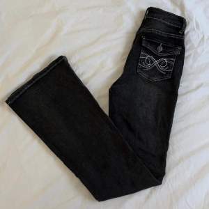 Bootcut jeans med detaljerade fickor. I färgen svart med toner av grå. De är i modellen bootcut. De är i passformen midwaist. Bra stretch. De är i nyskick. Storlek 34. 💗  Midjemått: 67 cm Innerbenslängd: 78 cm Totallängd: 106 cm Lårvidd: 22 cm