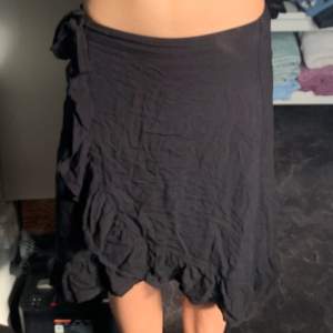 Svart kjol med volang och knytning från Lindex. Använts flitigt men i bra skick förutom en liten fläck längst ner på kanten. Skriv om du undrar nåt😊Midjemått: 30 cm men har resor på baksidan Längd: ca 50 cm