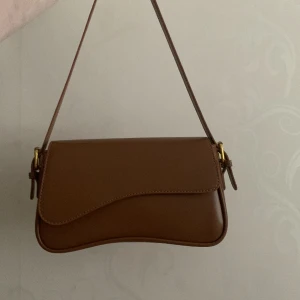 Handväska brun - Helt oanvänd handväska o brun färg och jätte bra kvalitet💛 kommer med anpassningsbara remmar och en ficka på insidan! säljes då jag inte använder handväskor längre🥰