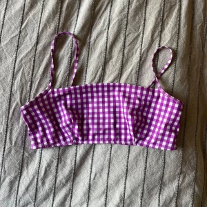 Lila rutig bikini från Weekday - En lila rutig bikiniöverdel från Weekday. Överdelen har smala axelband och ett rutigt mönster i lila och vitt. har en matchande underdel