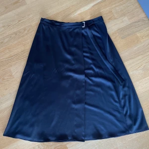 Kjol  - En svart omlottkjol i ett glänsande material från H&M. Den är i vadlång och faller väldigt snyggt. Något liten i storleken, använd med i bra skick. 