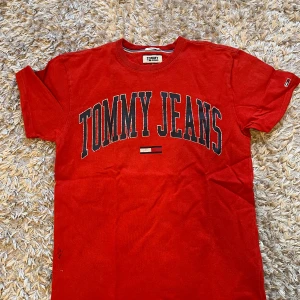 Röd Hilfiger T-shirt - Röd Tommy Hilfiger tisha i storlek S, säljer då den blivit för liten för mig. Skick 7/10 då det kommit svart färg på höger sida av tröjan (se bild 4) Hör av dig vid eventuella frågor! 🙌🏻