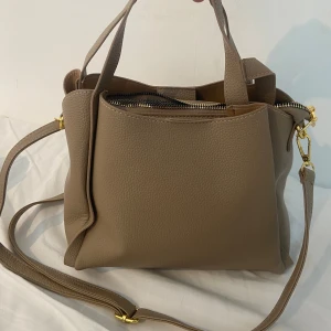 Väska - Biege väska med gulddetaljer. Jättefin men i helt nytt oanvänt skick! Får plats med såå mycket!