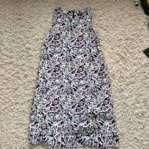 Mönstrad klänning från Koul Edition - En ärmlös klänning från Koul Edition med ett abstrakt mönster i svart, vitt, rosa och blått. Klänningen har en rak passform och är knälång.