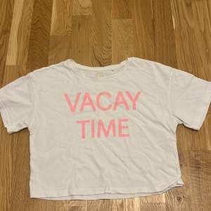 En vit t-shirt från Cool Club med texten 'VACAY TIME' i rosa på framsidan. T-shirten har korta ärmar, en rund halsringning och den är litr croppad.