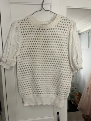 Vit stickad topp från Zara - Supersöt vit stickad topp från Zara med korta puffärmar i broderad spets och ett hålmönstrat framstycke. Rund halsringning och ribbade muddar ger en chill men ändå stylish vibe. Perfekt för dig som vill ha något unikt och luftigt till sommaren! Passar även xs 