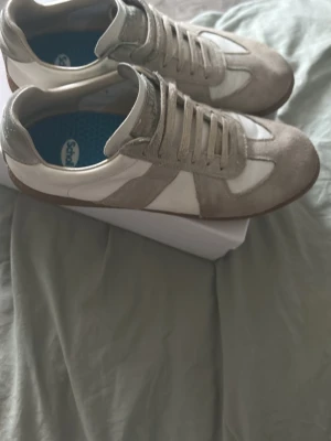 Maison margiela skor   - Säljer ett par stilrena sneakers i märke Maison margiela. Skorna har matchande beige snörning och en enkel, tidlös design som passar till det mesta. Perfekta för dig som gillar minimalistisk stil. Väldigt praktiska skor skulle jag säga och väldigt stiliga. Sitter även ett par andra sulor för på dom just nu men kan tas bort ifall man vill de. Skick 7.5 /10 skriv för intresse kan även gå ner i pris vid snabbaffär. 