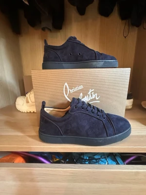 Mörkblå sneakers från Christian Louboutin - Snygga mörkblå sneakers i mocka från Christian Louboutin med klassisk röd sula och svarta snören. Lågt skaft och stilren design som passar perfekt till streetwear eller en mer uppklädd look. Ikonisk signatur under sulan för extra attityd.