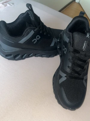 Svarta On Running sneakers - Snygga svarta sneakers från On med grå detaljer och sportig design. Ovandelen är i mesh och syntetmaterial för bra andningsförmåga. Sulan har On's unika CloudTec-teknologi för extra komfort och dämpning. Perfekta för dig som gillar stilrena och funktionella skor. De kanske ses att det är använd på grund de ser ut att de dammigt men den är aldrig använt ute den har ba blivit testat sen i garderoben  