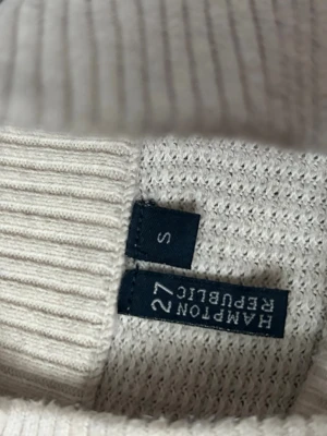 Vit stickad tröja Hampton Republic - Snygg vit stickad tröja från Hampton Republic med halv dragkedja framtill och ribbade muddar vid ärmslut och nederkant. Tröjan har en klassisk passform och är perfekt för lager på lager. Materialet känns mjukt och bekvämt.