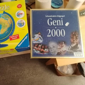 Geni 2000 frågespel & 3D globpussel - Säljer sällskapsspelet Geni 2000 och ett Ravensburger 3D pussel i form av en jordglob. Frågespelet har blå förpackning och globpusslet har gul kartong med illustration av en jordglob och papegoja. Perfekt för spelkvällar och kluriga utmaningar.