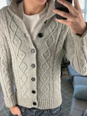 Ljusgrå kabelstickad kofta - Otroligt snygg grå cardigan i riktigt bra skick! Inga defekter förutom att tröjan är lite nopprig vilket man kan fixa själv, modellen på bilderna är 187, kan passa lite mindre också och bara höra av sig vid frågor och funderingar! Pris kan diskuteras! Mått A:48 cm B:45 cm C:41 cm D:66 cm
