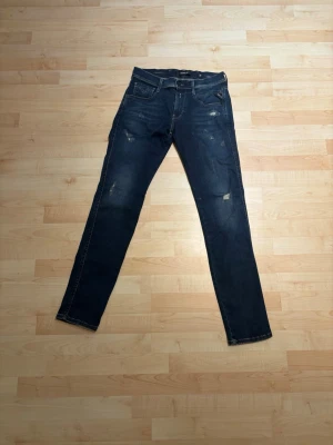 Mörkblå Replay jeans  - Säljer ett par mörkblå slim fit jeans från Replay, modell Hyperflex. Jeansen har snygga slitningar och tvättade detaljer, fem fickor och klassisk knappgylf. Perfekta för dig som gillar en trendig och avslappnad stil.