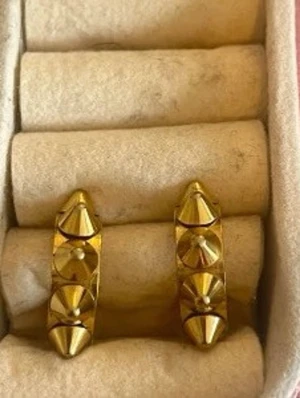 Guldiga örhängen med nitar - Coola örhängen i guldfärgad metall med markerade konformade nitar runt hela ringen. De har en chunky design och är perfekta för dig som gillar att sticka ut med accessoarer. Säljs som ett par.
