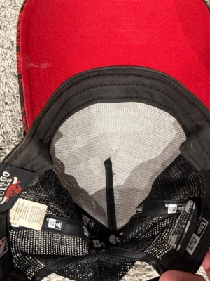 Chicago Bulls röd och svart keps - Snygg keps i rött och svart med Chicago Bulls-logga. Kepsen har böjd skärm och mesh på baksidan för extra ventilation. Justerbar passform och broderade detaljer. Perfekt för dig som gillar basket och streetwear.