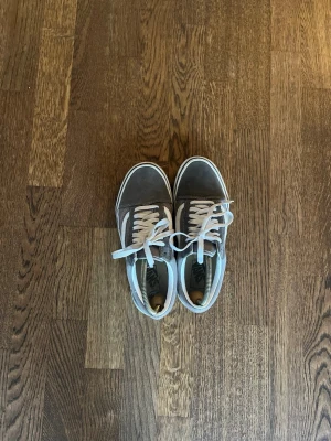 Gråa Vans Old Skool sneakers - Säljer ett par klassiska Vans Old Skool sneakers i grått med vit sula och vit sidostripes. Skorna har snörning och är tillverkade i en kombination av mocka och canvas. Perfekta för en avslappnad streetwear-look.