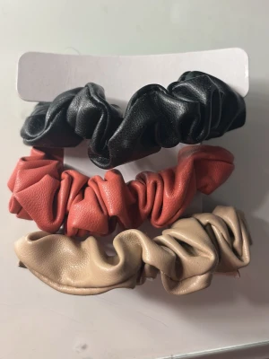 3-pack scrunchies i fejkläder - Säljer ett 3-pack scrunchies i fejkläder med coola färger: svart, korallrosa och beige. Oanvända💕