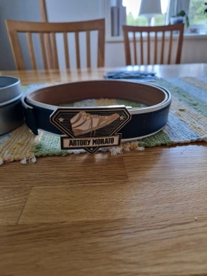 Svart skärp från Antony Morato XL - Stilrent svart skärp från Antony Morato i äkta skinn med en unik och snyggt designad metallspänne. Skärpet har ljus insida och tydlig logga på spännet. Perfekt accessoar för att lyfta din outfit.
