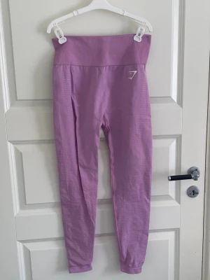 Lila seamless tights från Gymshark - Snygga lila seamless tights från Gymshark med hög midja och diskret logga på låret. Tightsen har ribbade detaljer och är tillverkade i ett stretchigt material som passar perfekt för träning och gym.