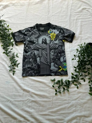 Svart Brasilien fotbollströja - Unik svart fotbollströja med tryck av Kristusstatyn och brasilianska symboler. Tröjan har detaljer i gult och grönt, samt Brasilien-emblem på bröstet och ryggen. Tillverkad i ett lätt och snabbtorkande material, perfekt för träning eller match.