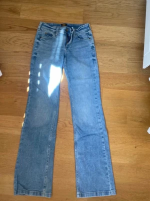 Ljusblå bootcut jeans från Lee - Säljer ett par ljusblå bootcut jeans från Lee med klassisk femficksmodell och Lee-logga på bakfickan. Jeansen har normal midja och är tillverkade i denim med lätt tvättad look. Perfekta för en avslappnad och trendig stil.