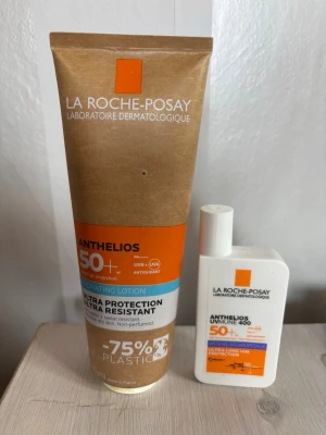 La Roche-Posay Anthelios solskydd - Två solskyddsprodukter från La Roche-Posay Anthelios-serien, båda med hög solskyddsfaktor (SPF 50+). En brun tub och en vit flaska, båda med orange detaljer. Passar för dig som vill ha effektivt skydd mot UVA och UVB.