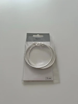Stora silvriga hoops örhängen - Säljer ett par stora, runda hoops i silverfärg från Appear. Örhängena har små diamanter längs hela ringen som ger extra bling. Aldrig använda💕