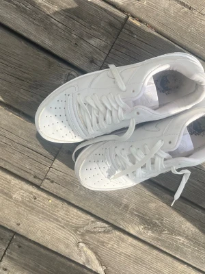 Helvita sneakers med klassisk design - Säljer ett par helvita sneakers med lågt skaft och klassisk siluett. Skorna har perforerad tå, vita skosnören och sula i gummi. Materialet är en mix av läder och syntet. Perfekta för dig som gillar en clean och stilren look.