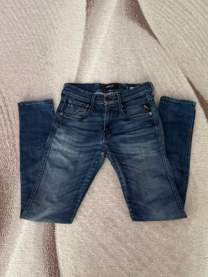 Blå slim fit jeans från Replay - Snygga blå slim fit jeans från Replay med klassisk femficksdesign och diskreta slitningar framtill. Jeansen har normal midja, dragkedjegylf och är tillverkade i ett mjukt denimtyg som ger en bekväm passform. Priset är inte skrivet i sten!