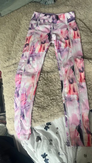 Färgglada träningsleggings med mönster - Säljer ett par snygga träningsleggings med abstrakt mönster i rosa, lila, vitt och röda toner. De har hög midja och sömmar längs benen för extra passform. Perfekta för gymmet eller löprundan och tillverkade i stretchigt material. Pris diskuteras