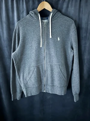 Grå zip hoodie från Polo Ralph Lauren - 📍Storlek:M  💪🏽Skick:Mycket bra   📐Mått:Längd:64:cm:Bred:50:cm:  📎Material:86%Bomull:14%polyester  📦Skickar alltid inom 48h  ✅Äkthetsgaranti   
